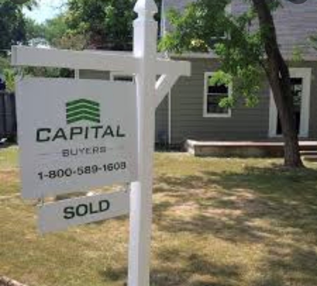 Real estate sign with "SOLD" displayed, advertising Capital Buyers, in front of a house with green landscaping. Highlights recent property sale.